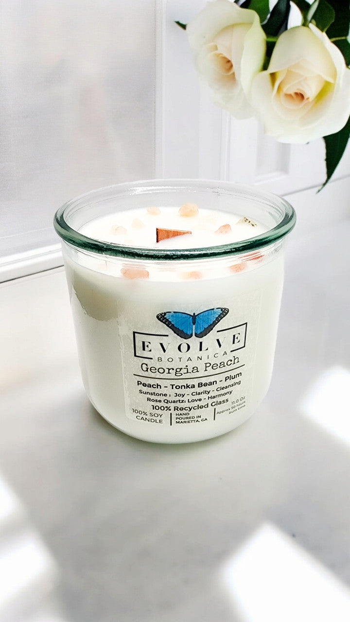 Evolve Botanica Rocks Candle with Georgia Peach scent, wood wick, gemstone, and soy wax, displayed in a clear glass jar.