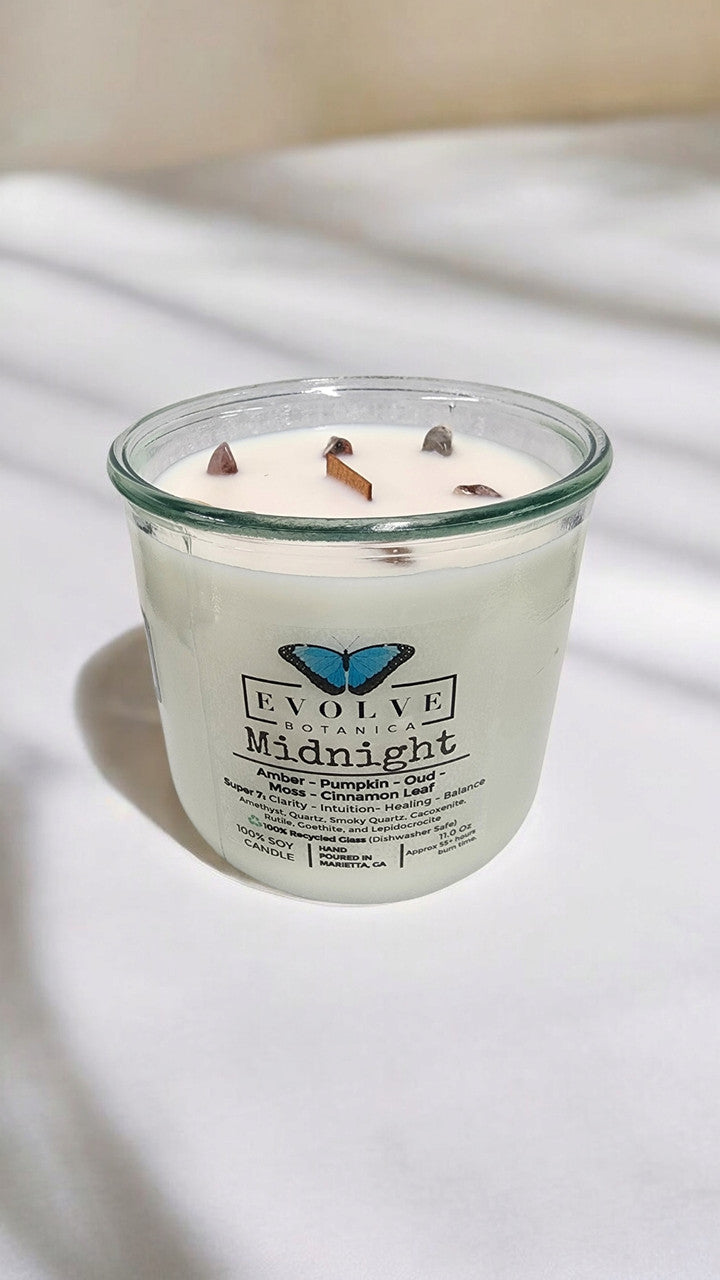 Evolve Botanica Midnight Rocks Candle with wood wick and seven gemstone soy candle in a dark jar.