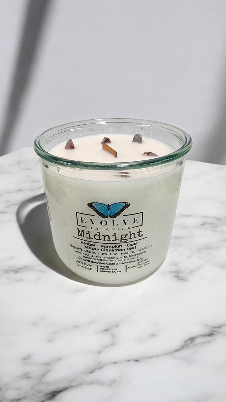 Evolve Botanica Midnight Rocks Candle with wood wick and super seven gemstone, soy wax, in a dark-colored container.