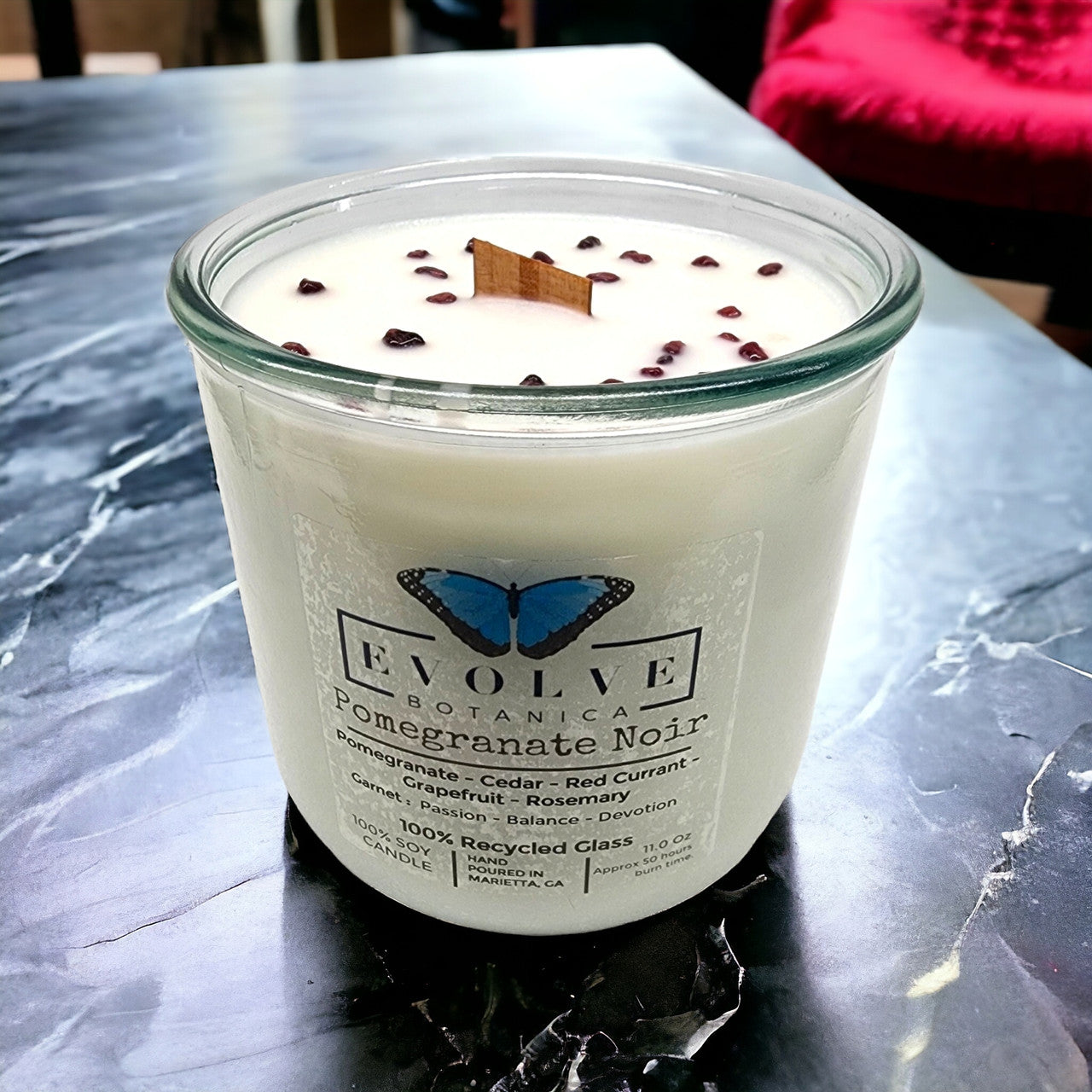 Evolve Botanica Pomegranate Noir Rocks Candle with wood wick, garnet gemstone, soy wax, in a decorative container.