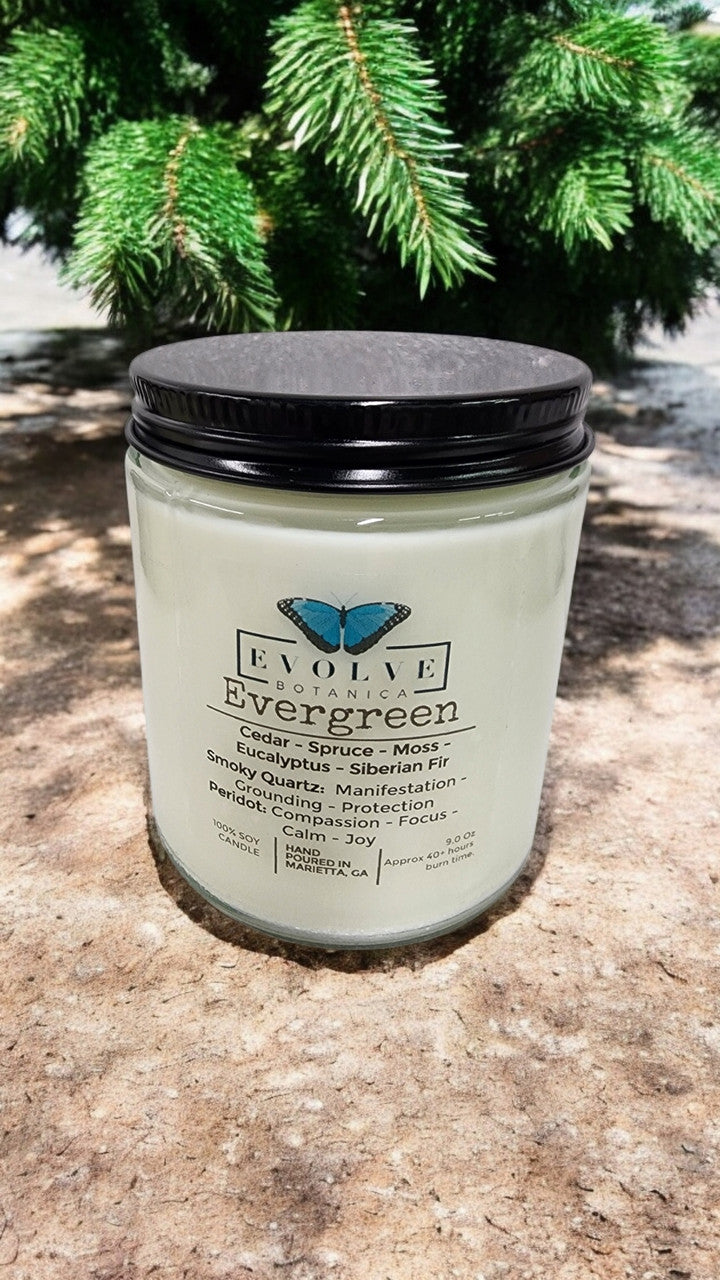 Evolve Botanica 9oz jam jar soy candle with evergreen scent, smoky quartz and peridot crystals, natural wood wick, and clear glass jar.