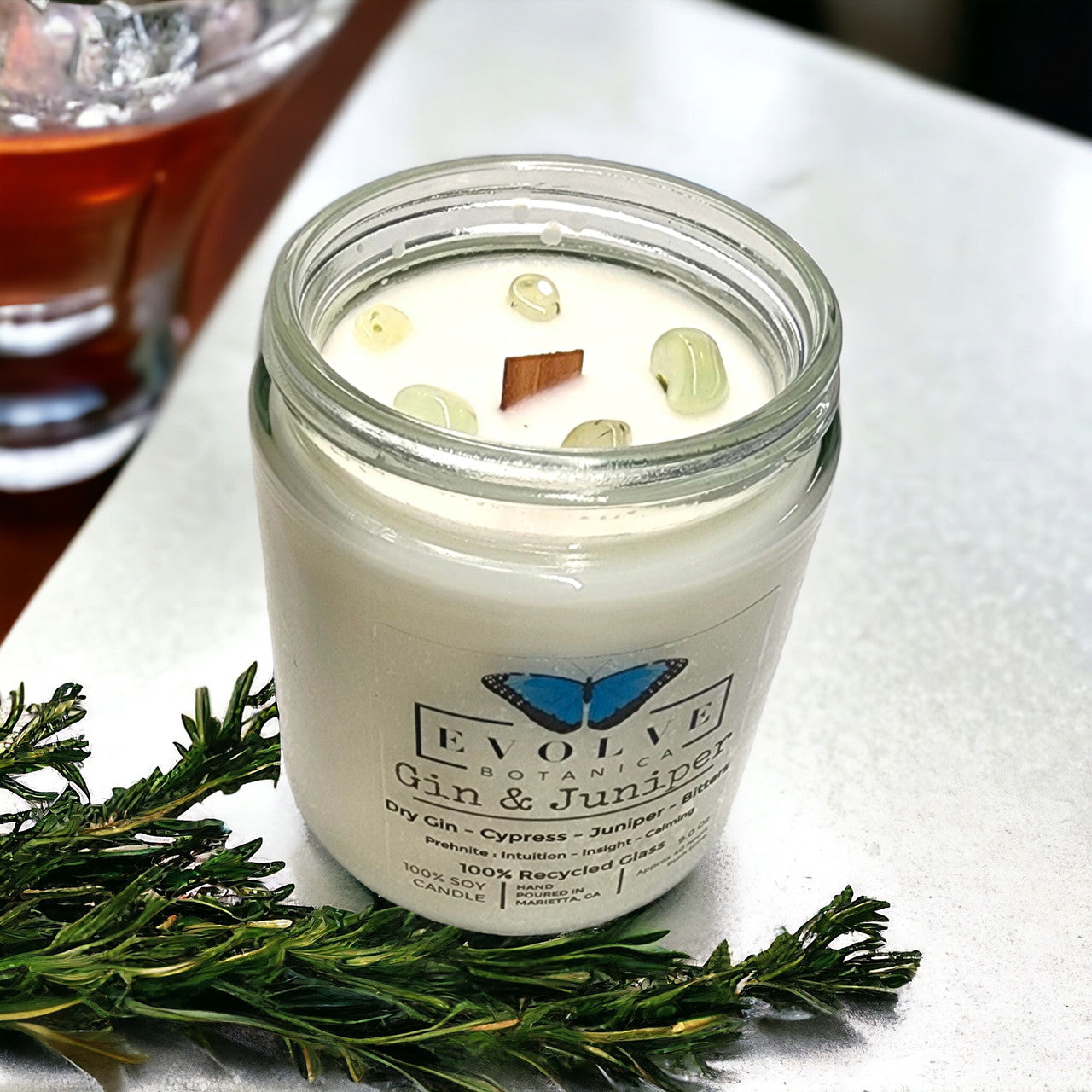 Evolve Botanica 9oz crystal soy candle in jam jar with gin and juniper scent, featuring a natural wood wick and prehnite gemstone.