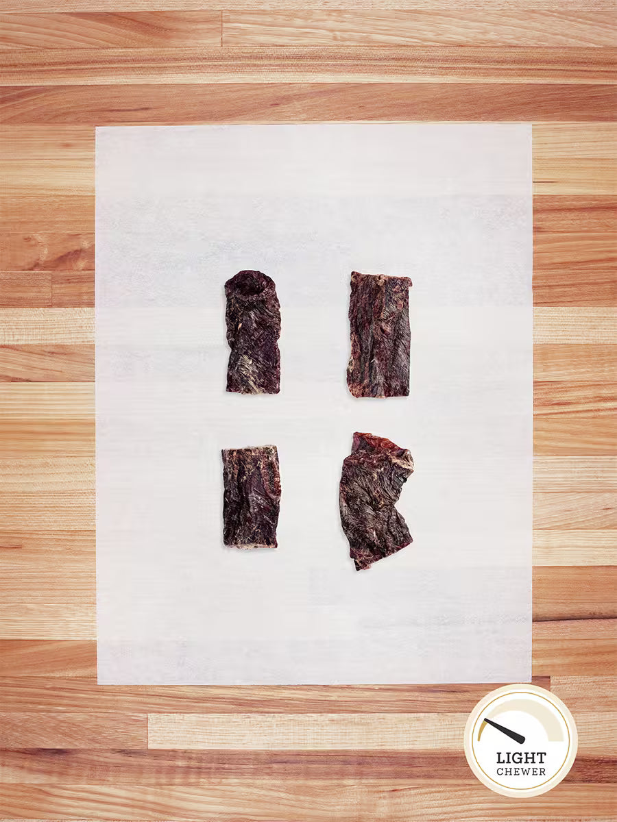 Four pieces of Farm Hounds Beef Weasand (Esophagus) from pasture-raised cattle are displayed on white parchment atop a wooden surface, with a circular Light Chewer label in the lower right corner.