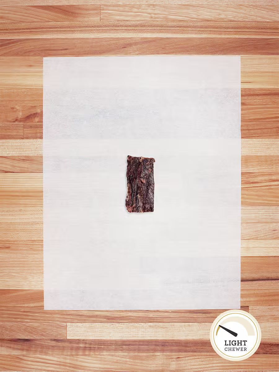 A single rectangular piece of Farm Hounds Beef Weasand - Esophagus, made from pasture-raised cattle, sits centered on a white sheet atop a wooden surface; a circular Light Chewer badge appears at the bottom right.