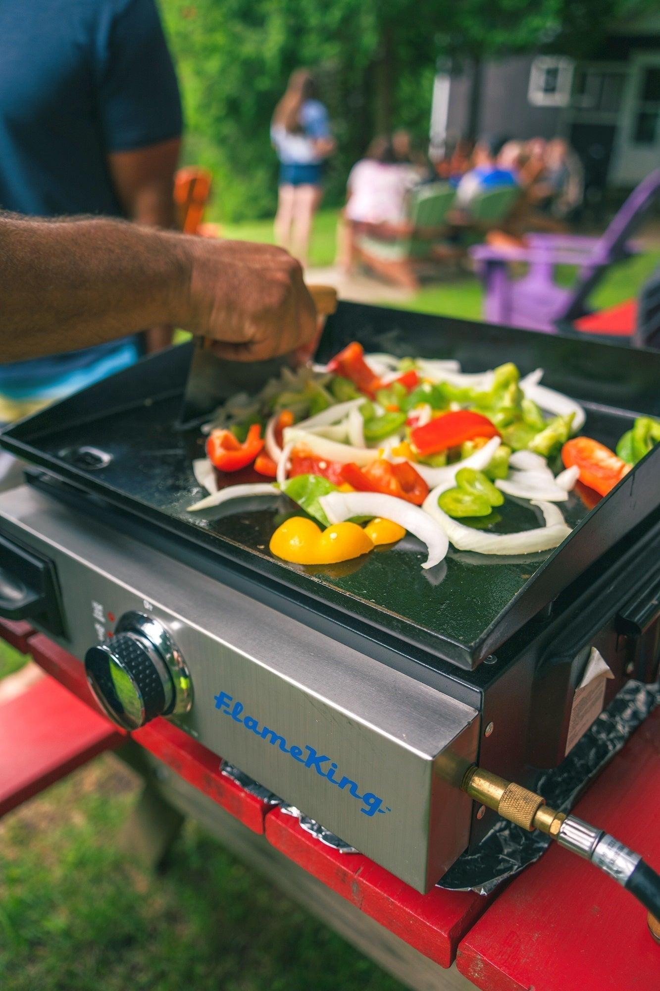 Portable Flame King cast iron flat-top grill and griddle for camping, showing the black cooking surface with handles and control knob.
