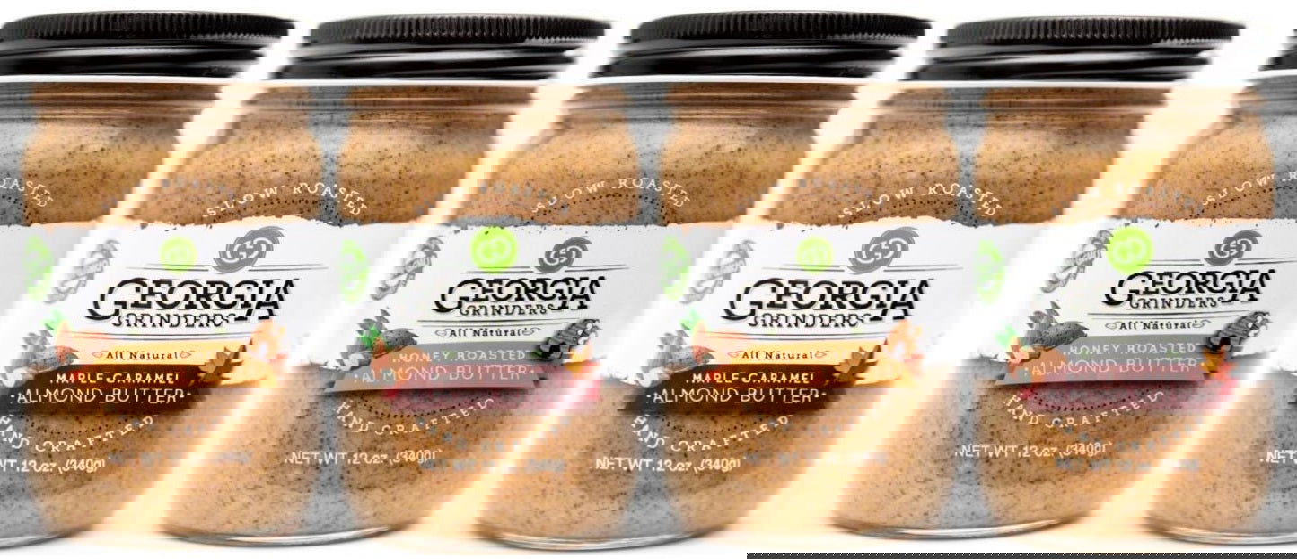 Four jars of Georgia Grinders Maple Caramel Almond Butter and Honey Roasted Almond Butter Mix Pack (two 12oz jars each) are shown side by side with black lids; the image is distorted with diagonal white lines.