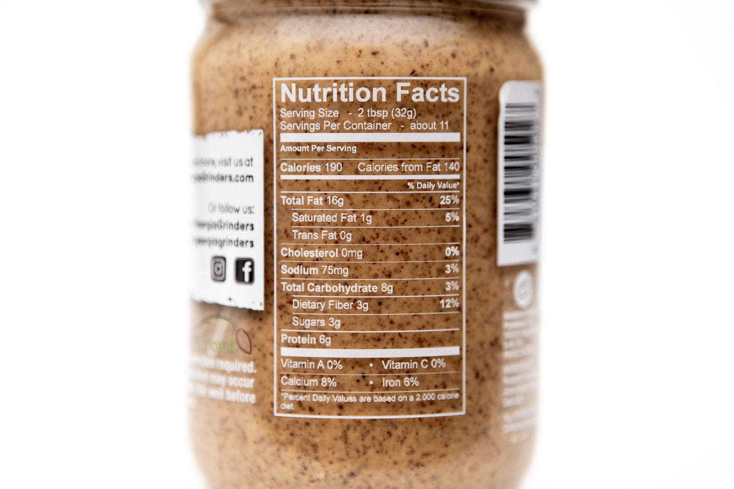 A close-up of a Georgia Grinders Maple Caramel Almond Butter and Honey Roasted Almond Butter Mix Pack jar displays its Nutrition Facts label with serving size, calories, fat, sodium, carbs, fiber, sugars, and protein on a white background.