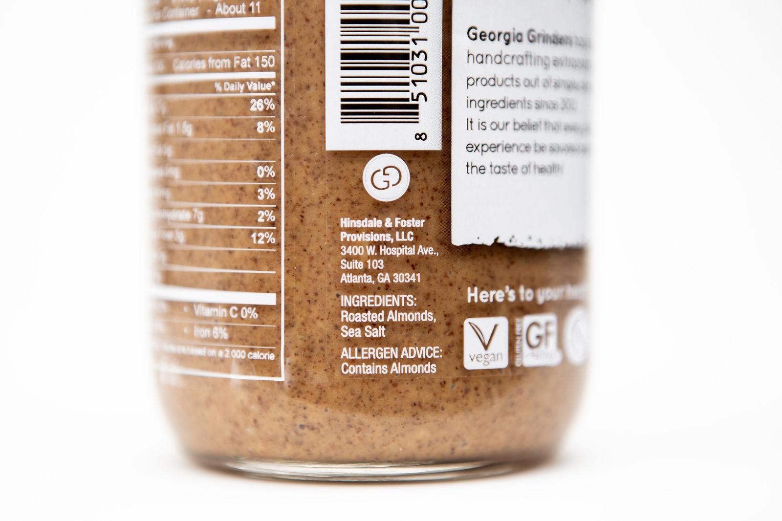 A close-up of a Georgia Grinders 12 oz WHOLE30 Nut Butter Assortment 4 Pack jar shows the ingredients, company address, barcode, and vegan and gluten-free symbols—ideal for those seeking WHOLE30-approved almond butter.
