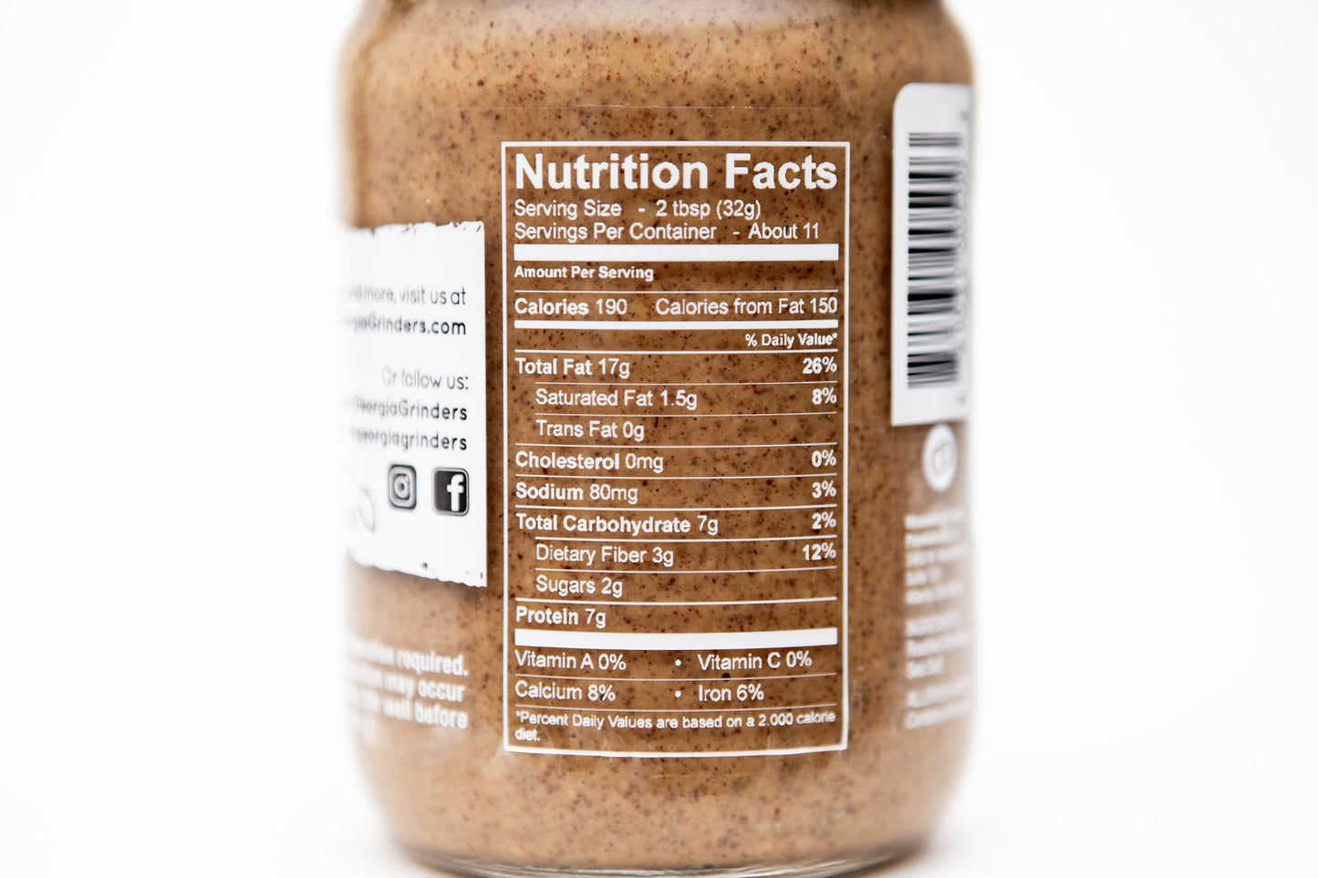 A close-up of the Georgia Grinders Cashew Butter nutrition label displays serving size, 190 calories per 2-tbsp serving, fat, sodium, carbs, sugars, protein details on a white background; the 12 oz jar has about 11 servings.