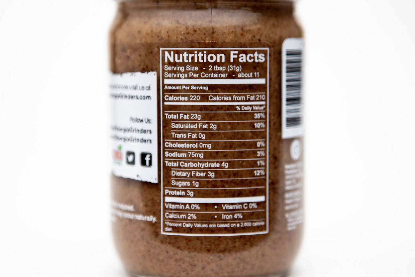 A close-up of the nutrition facts label on a Georgia Grinders 12 oz WHOLE30 Nut Butter Assortment jar, showing serving size, calories, fat, sodium, carbs, fiber, sugars, protein, vitamins, calcium & iron per serving.