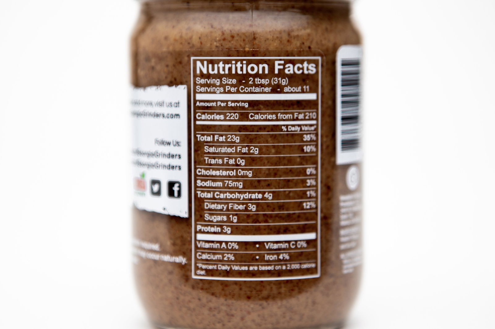A close-up of the nutrition facts label on a Georgia Grinders 12 oz WHOLE30 Nut Butter Assortment jar, showing serving size, calories, fat, sodium, carbs, fiber, sugars, protein, vitamins, calcium & iron per serving.