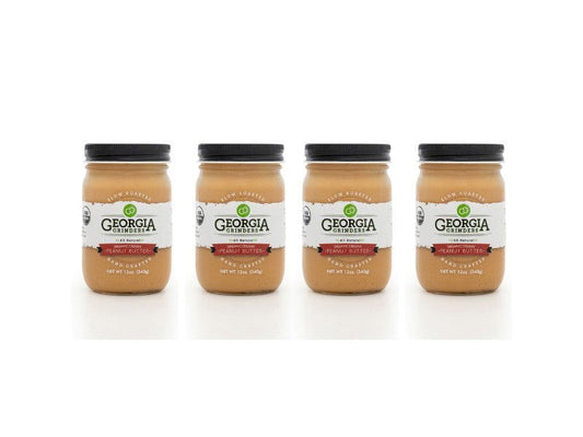 Four jars of Georgia Grinders Organic Creamy Peanut Butter 4 Pack (12 oz, CP-CL) are arranged in a row with black lids and white labels against a white background.
