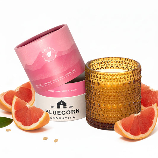 Bluecorn Candles Paloma scented candle in glassware with grapefruit aroma, showcasing a clear glass container with a lit wick.