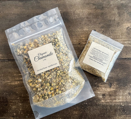 Dried organic chamomile herbs in a clear jar, showing small, golden-yellow flowers and leaves, from HerbalRoseApothecary.