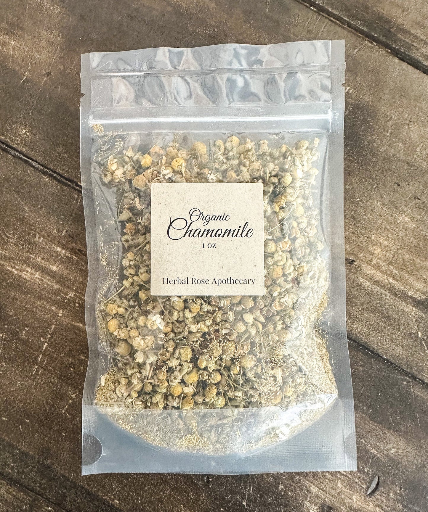 Dried organic chamomile herbs in a clear jar, showcasing small, dried flower buds from Herbal Rose Apothecary.