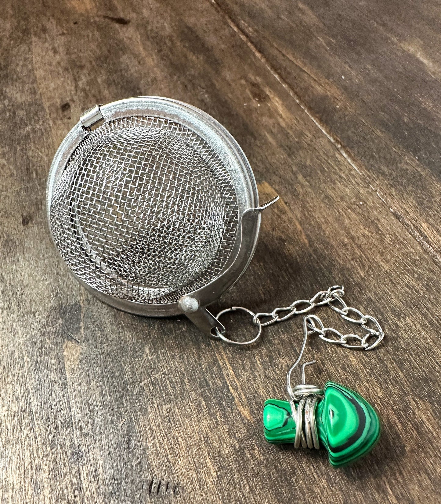 Herbalroseapothecary tea ball infuser with stainless steel mesh for brewing loose leaf tea in a teapot or cup.