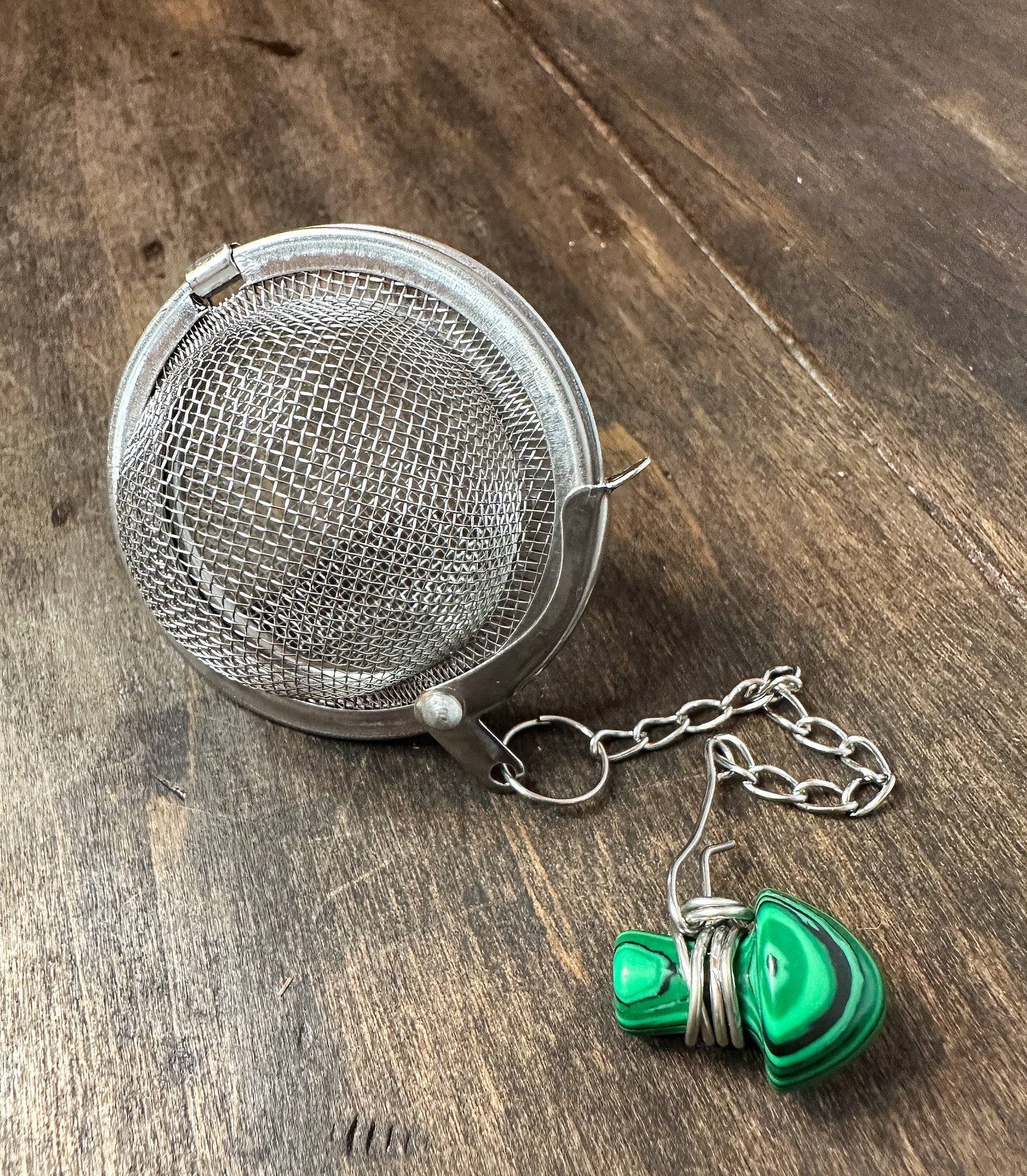 Herbalroseapothecary tea ball infuser with stainless steel mesh for brewing loose leaf tea in a teapot or cup.