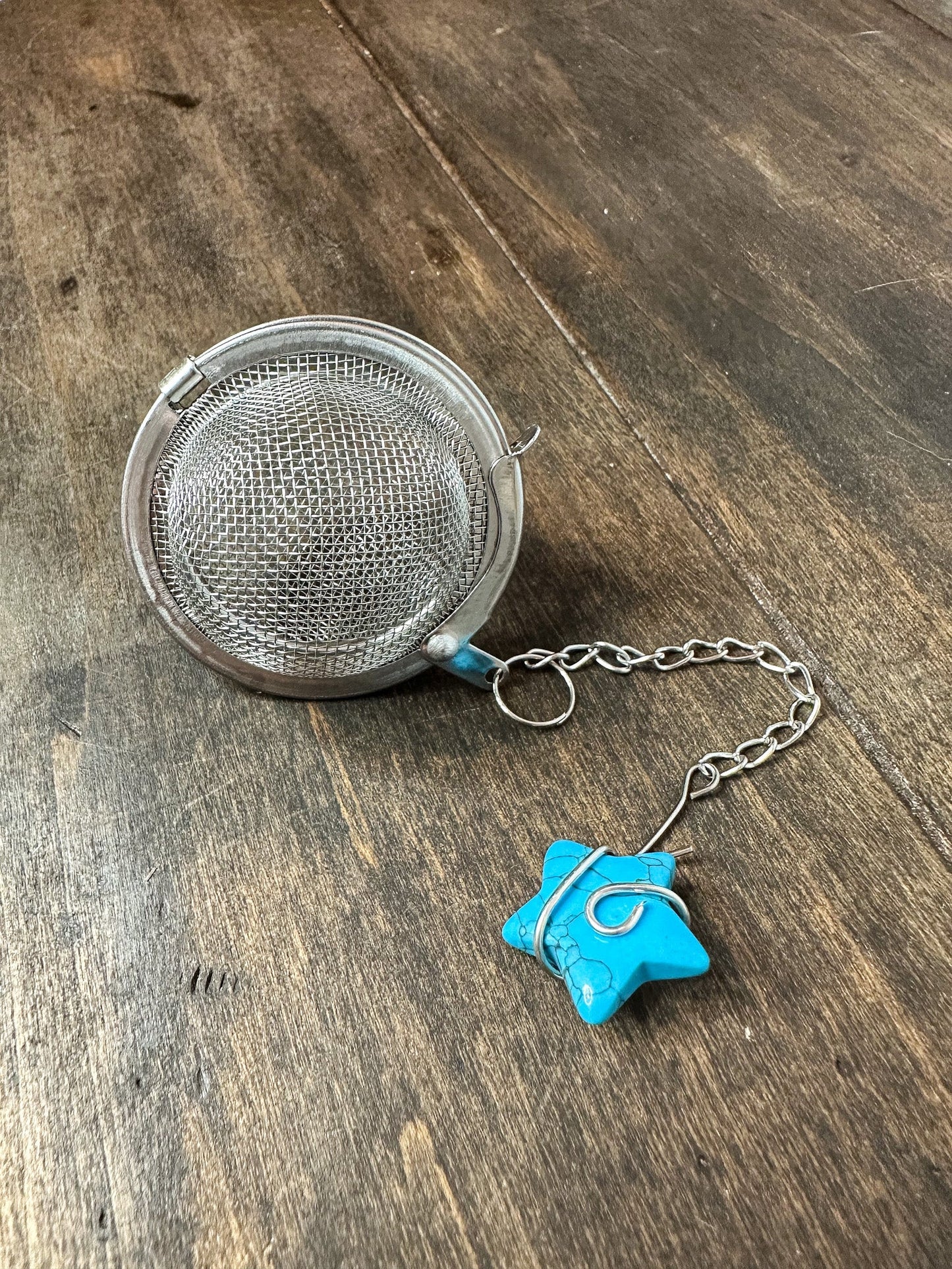 Herbalroseapothecary tea ball infuser with stainless steel mesh for loose leaf tea brewing in a teapot or cup.