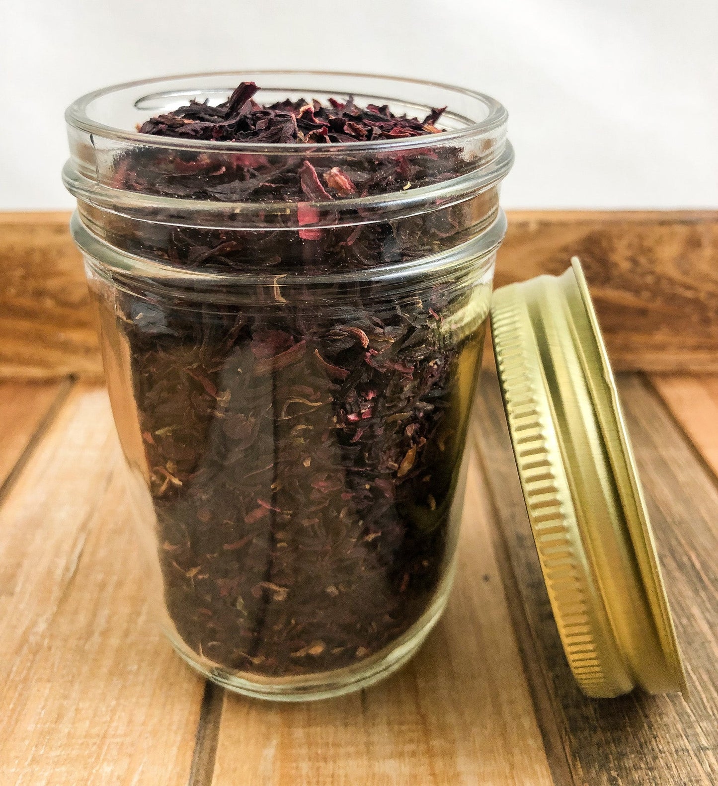 Small jar of dried hibiscus herbs from herbalroseapothecary, stored in a wood-colored and white herb jar.