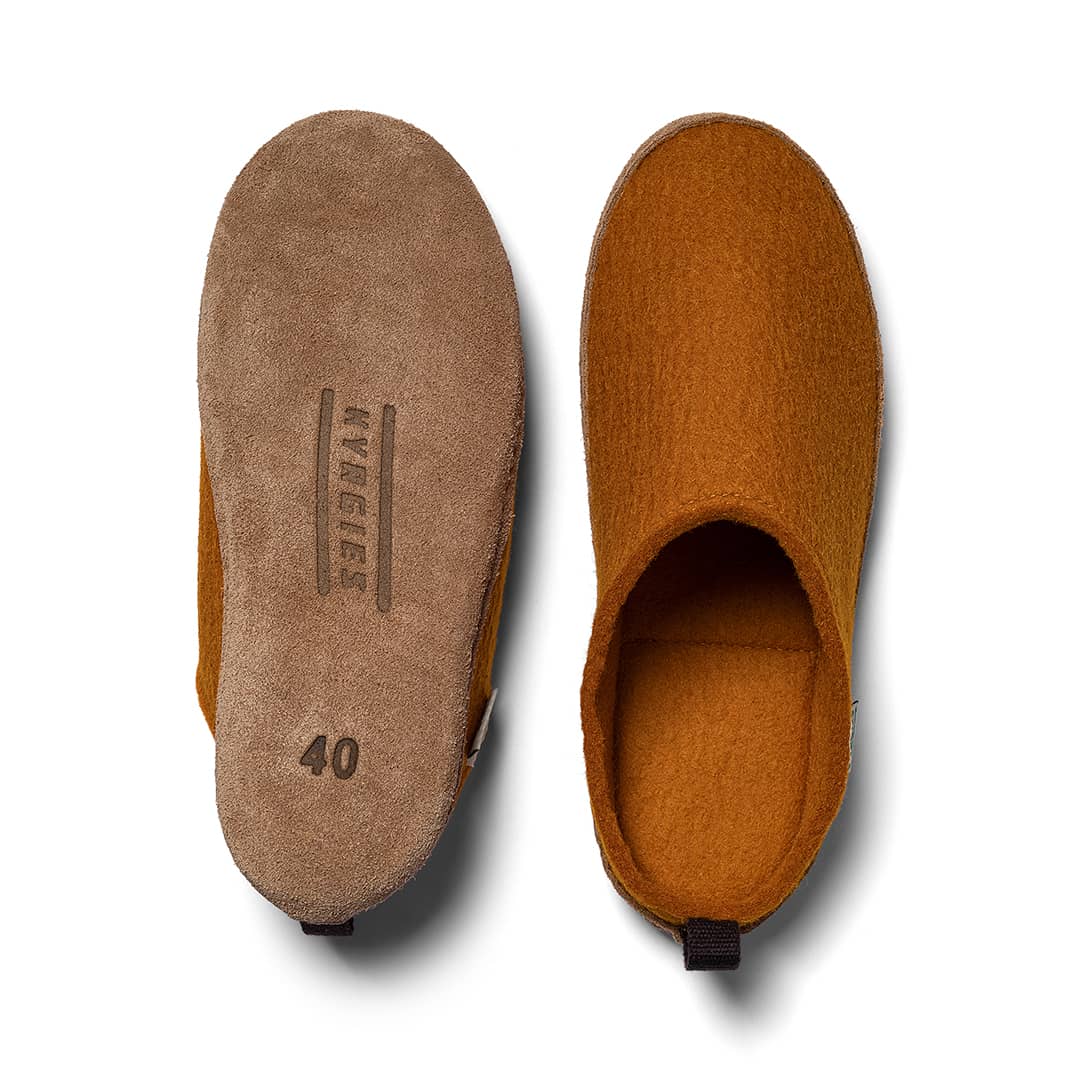 A pair of Kyrgies Indoor Wool Slides by Kyrgies is shown from above: the left slipper reveals the suede sole with MAGERS and size 40 printed, while the right displays the top and interior—these eco-friendly slides are naturally biodegradable.