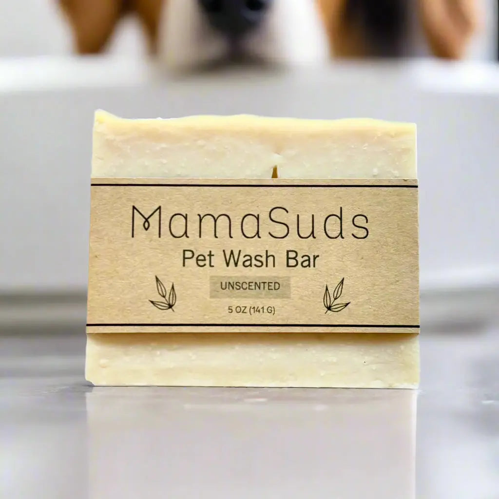 A natural-colored MamaSuds Pet Wash Bar Unscented, 5 oz (141 g), stands upright on a smooth surface with a blurred background; this vegan, gentle, and biodegradable soap offers safe care for your pet.