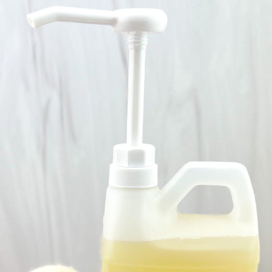 A close-up of a MamaSuds Soap Dispenser Pump filled with light yellow liquid, set against a softly blurred, light-colored background.