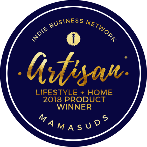 A round navy badge with gold and white text reads, INDIE BUSINESS NETWORK ARTISAN LIFESTYLE + HOME 2018 PRODUCT WINNER MAMASUDS, celebrating MamaSuds Laundry Detergent Soap. A small gold award icon is featured at the top.