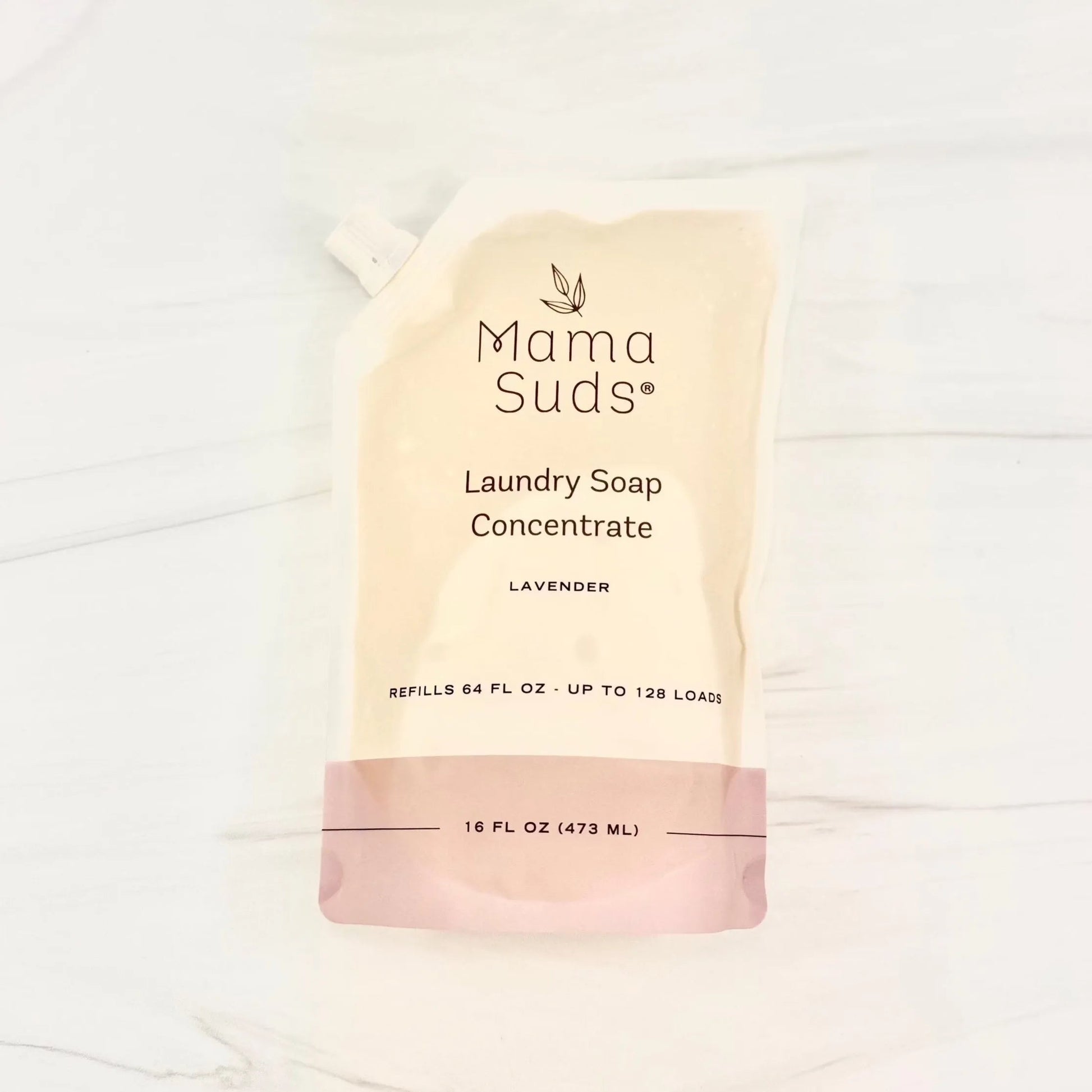 A recyclable MamaSuds Laundry Soap Concentrate Pouch in lavender (16 fl oz/473 ml) sits on a marble surface; this biodegradable formula refills 64 fl oz and provides up to 128 eco-friendly loads.