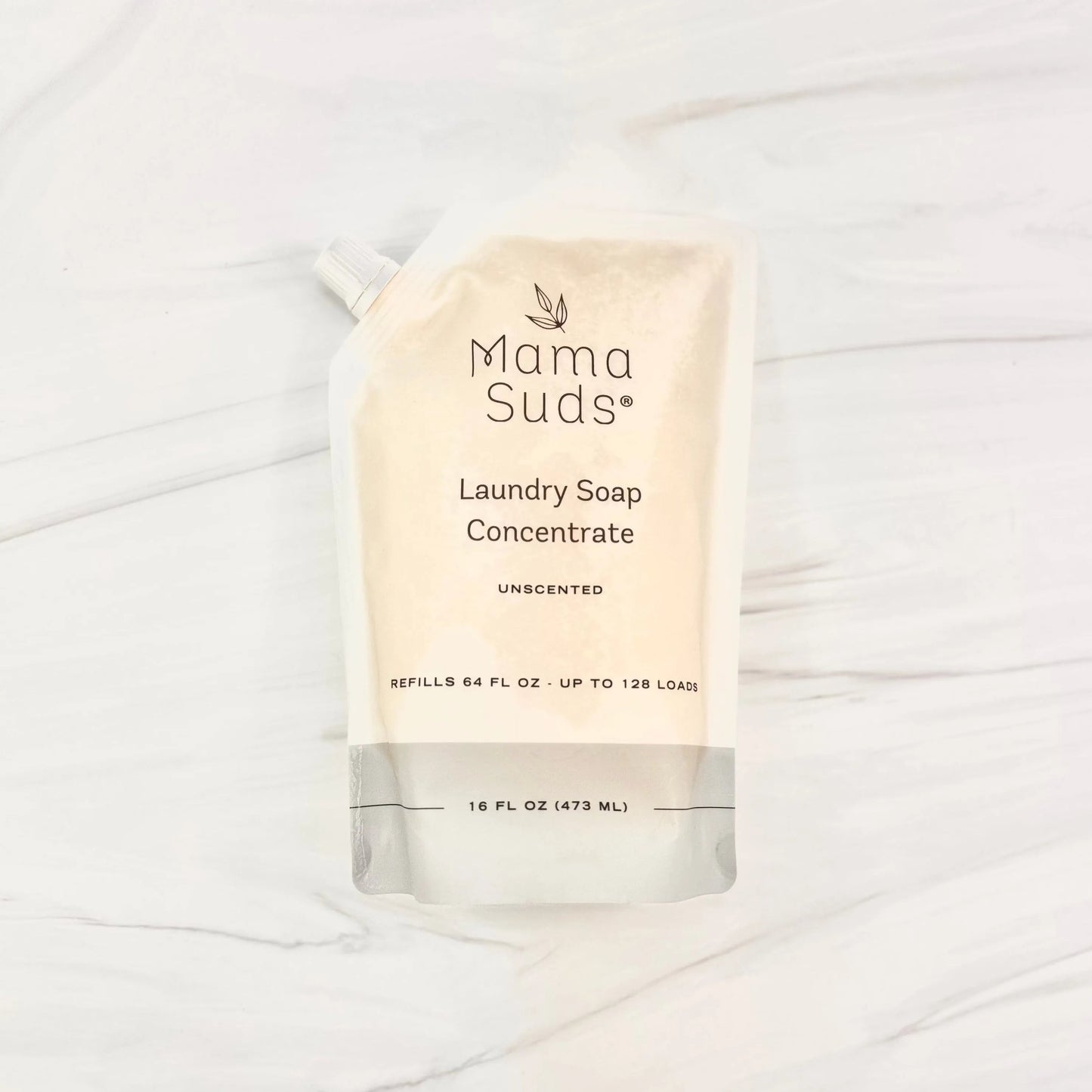A stand-up, recyclable pouch of MamaSuds Laundry Soap Concentrate (unscented, 16 fl oz/473 ml) is pictured on a light marble surface. The package states it refills 64 fl oz and is good for up to 128 loads.