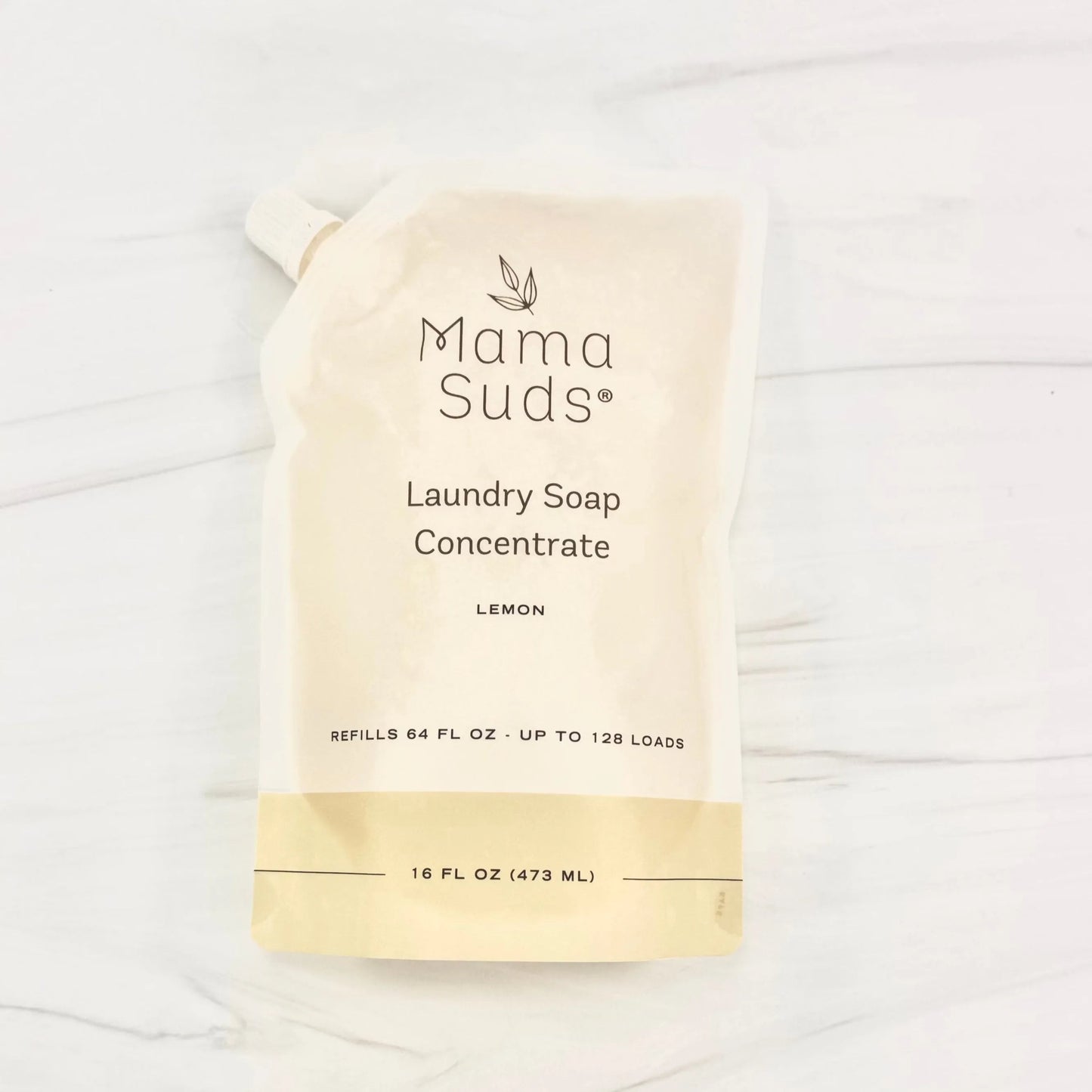 A 16 fl oz (473 ml) MamaSuds Laundry Soap Concentrate Pouch in lemon scent on a light, marble-like surface; the biodegradable, recyclable pouch refills up to 128 loads.