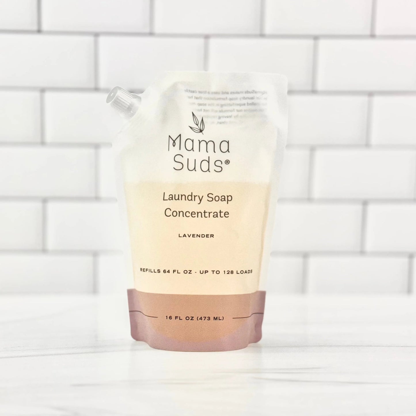 A stand-up, recyclable MamaSuds Laundry Soap Concentrate Pouch in lavender scent, with a spout and minimalist label, rests on a white tiled surface.