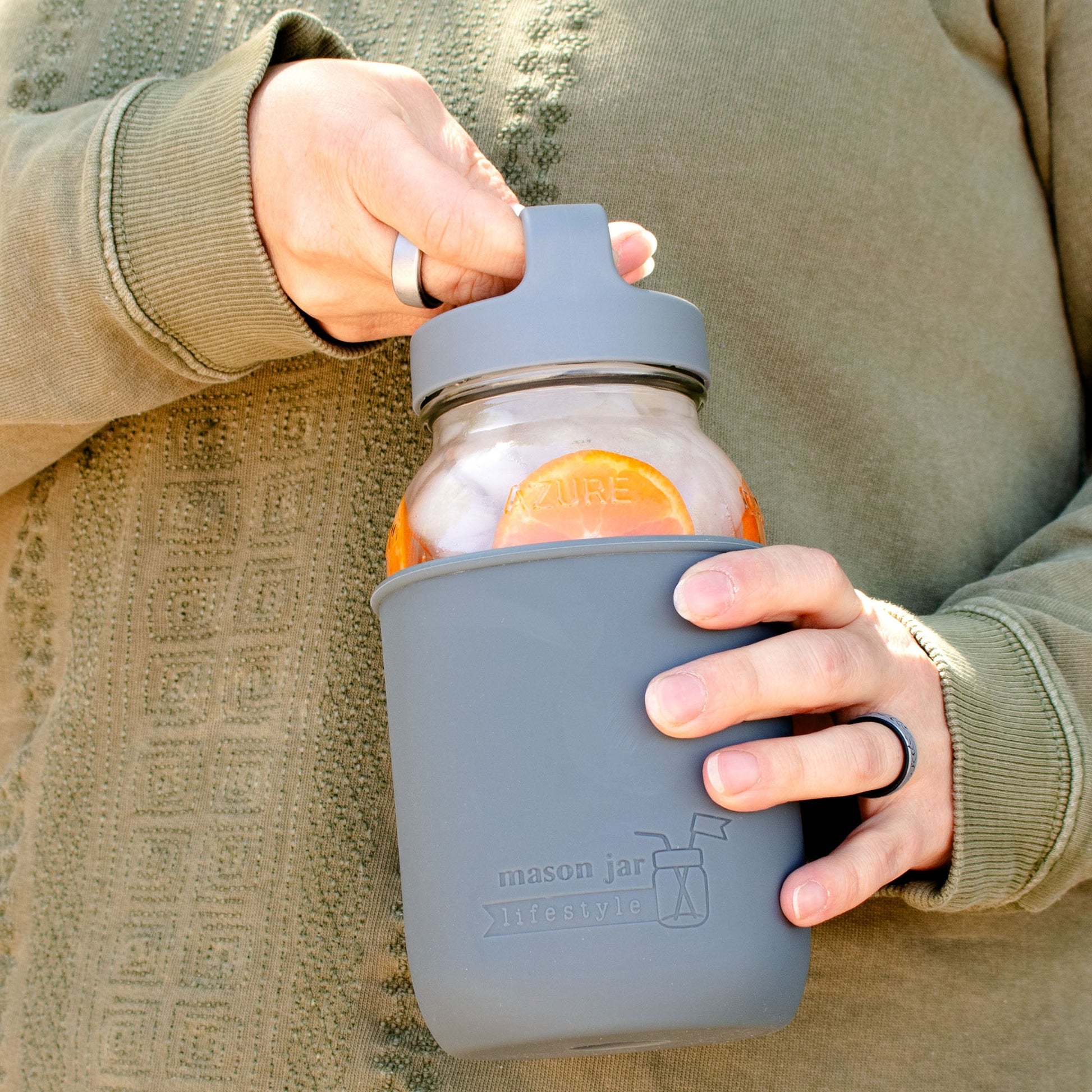 Mason Jar Lifestyle 32oz glass water bottle with silicone sleeve, carry handle, and lid, shown outdoors in azure color.