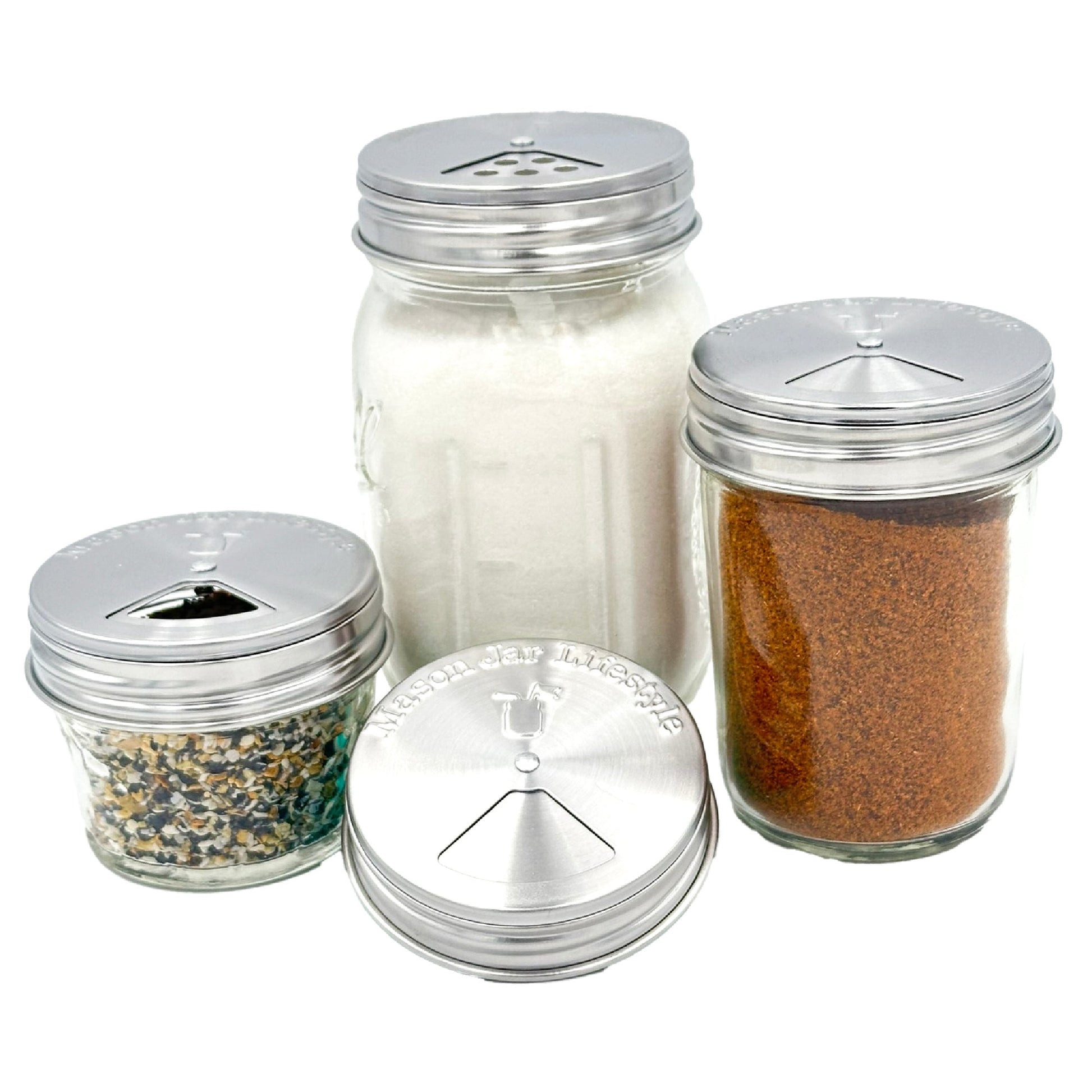 The Mason Jar Lifestyle Spice Shaker Stainless Steel Lids for Mason Jars 4 Pack let you season with white salt, reddish-brown spice, and mixed seeds; one lid is shown empty. These adjustable lids are dishwasher safe for easy cleaning.