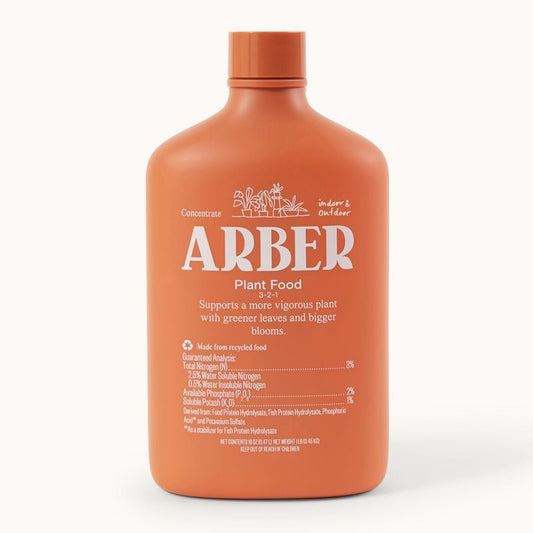 An orange bottle labeled Arber Organic Plant Food shows product details. This concentrate enhances soil fertility for indoor plants, promoting greener leaves and bigger blooms.