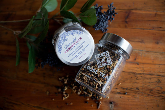 Glass jar of Piper and Leaf Elderberry Elixir loose leaf tea, showing dark dried elderberries and tea leaves inside.