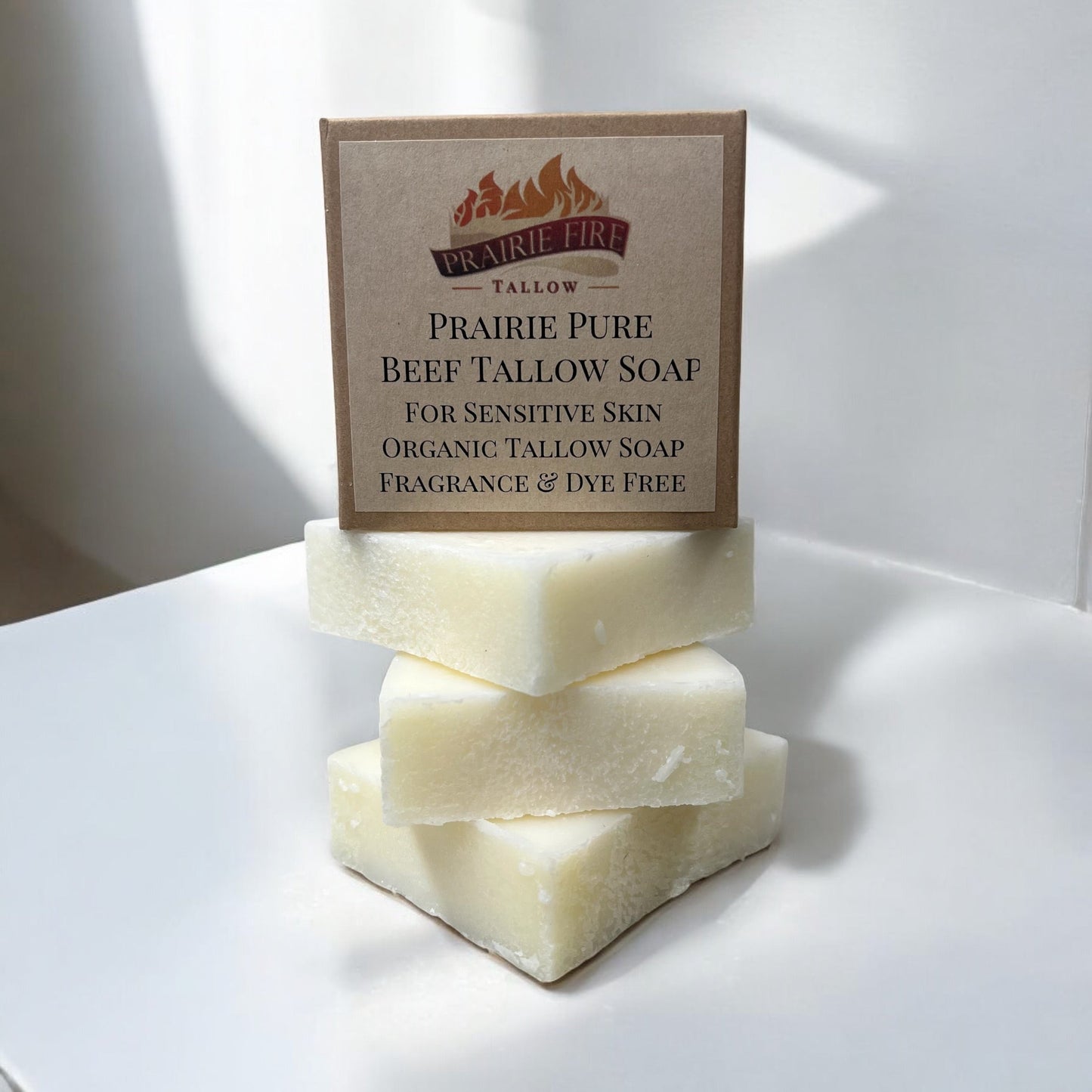 Three pale rectangular bars of Prairie Fire Tallow Pure Beef Tallow Soap (3 Pack) are stacked on a white surface, with a brown package on top describing the natural, organic, grass-fed soap as fragrance-free and suitable for sensitive skin.