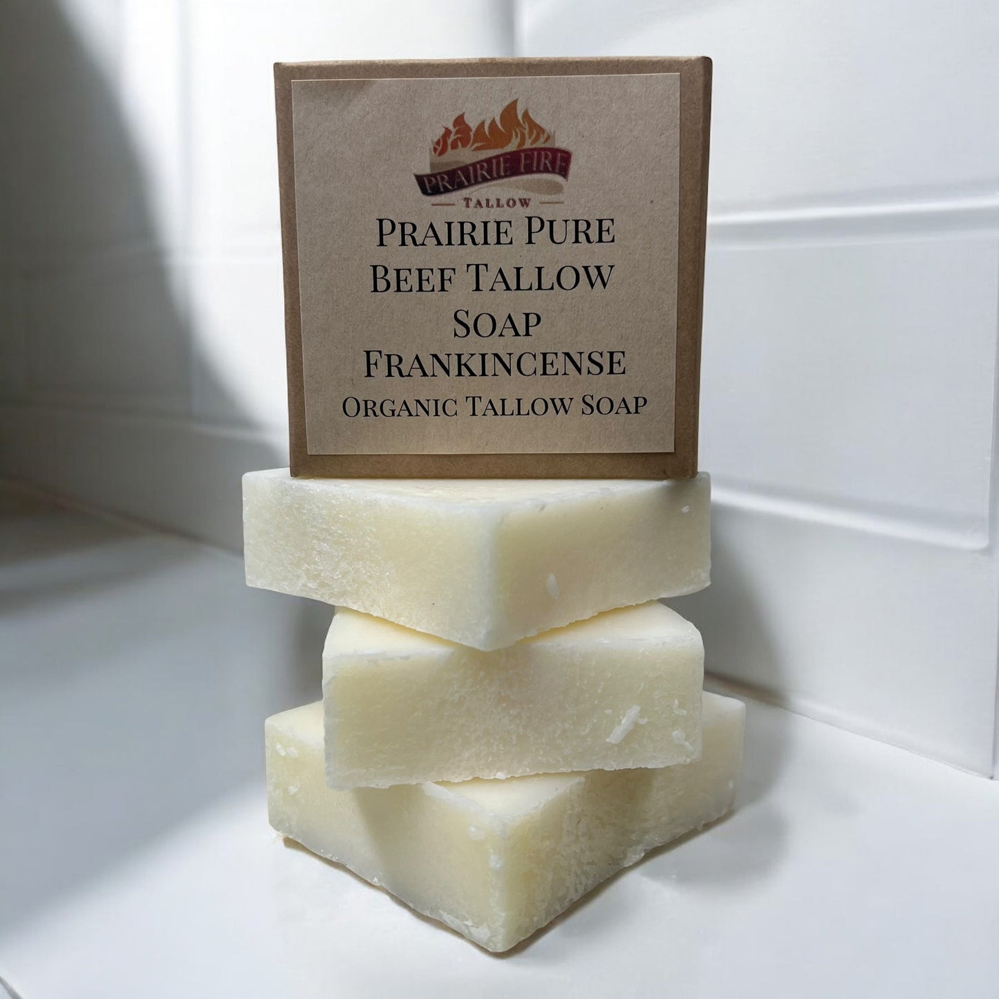 Three Prairie Fire Tallow Pure Beef Tallow Soap Bars (3 Pack, Made in USA) are stacked with a fourth in a box, set against white tiles. These natural, grass-fed soaps cleanse, moisturize, soothe, and hydrate face, body, and hair.