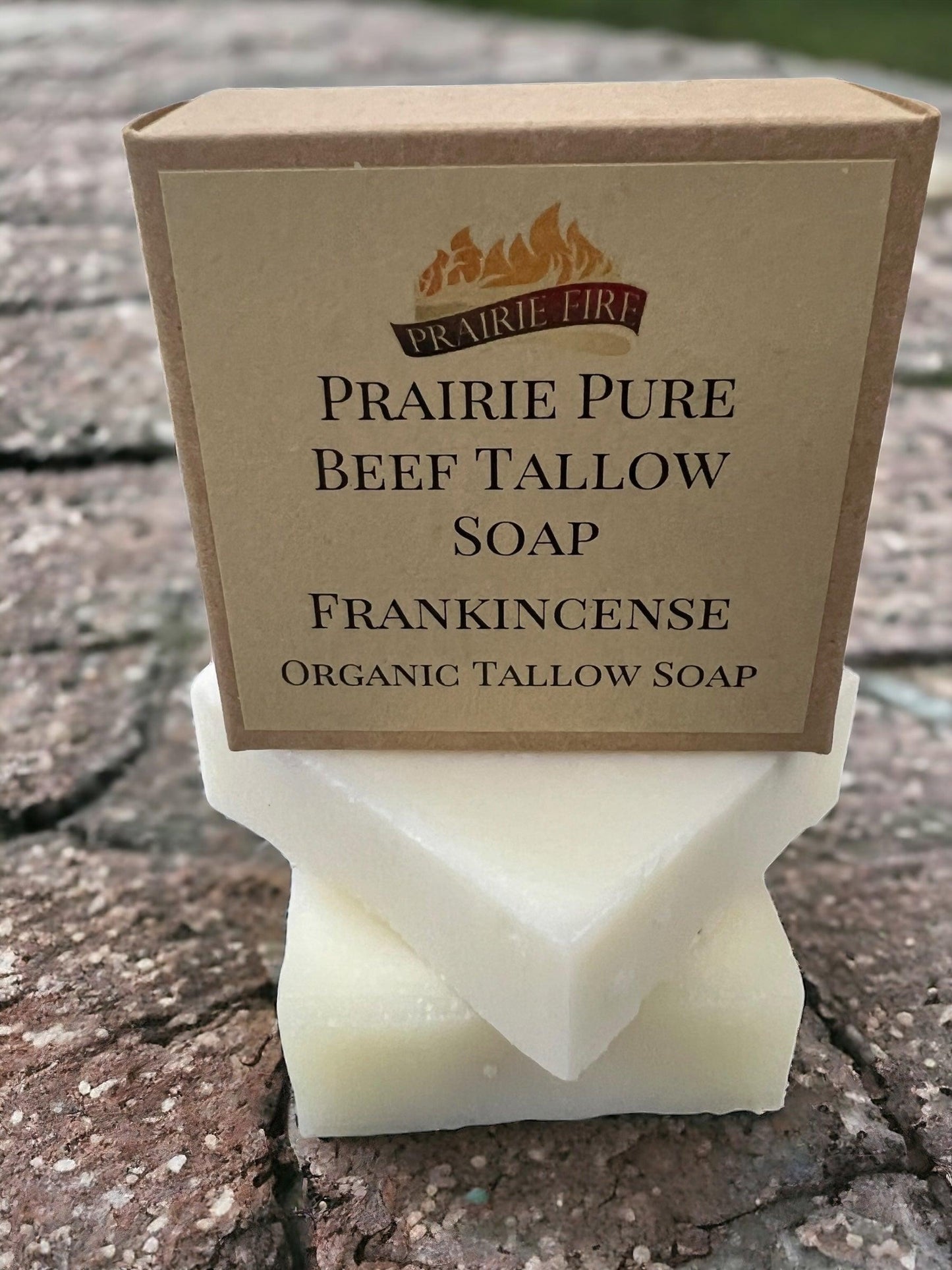 A box of Prairie Fire Tallow, Candles, and Lavender Pure Beef Tallow Soap Bar (3 Pack) sits atop two stacked white soap bars on a textured stone surface. The organic soap is grass fed/finished and made in the USA.