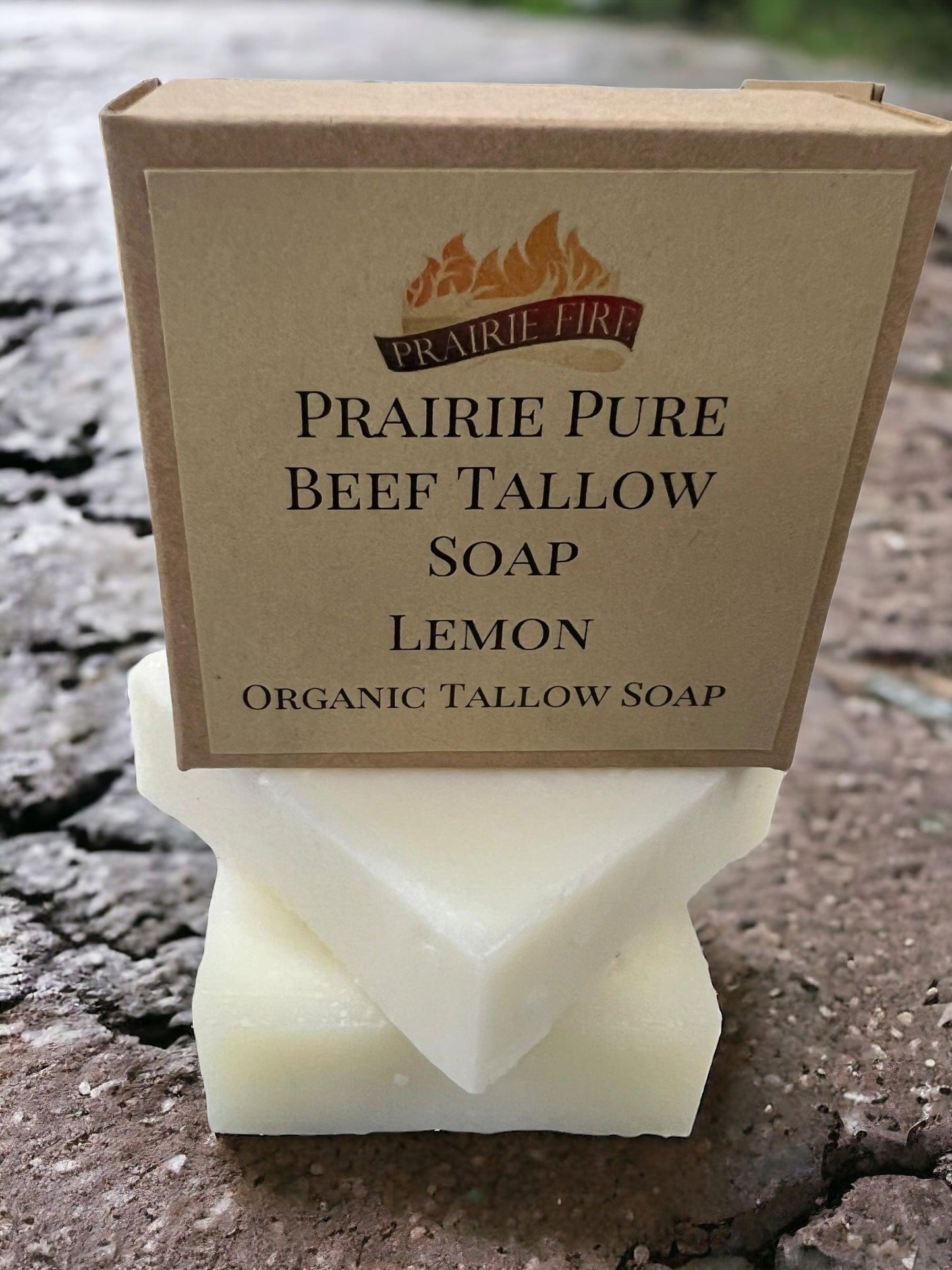 A box of Prairie Fire Tallow Pure Beef Tallow Soap Bar (3 Pack)—natural, organic, grass-fed—rests on two white bars with a textured stone background. Made in the USA for face, body, and hair: cleanses, moisturizes, soothes, hydrates.