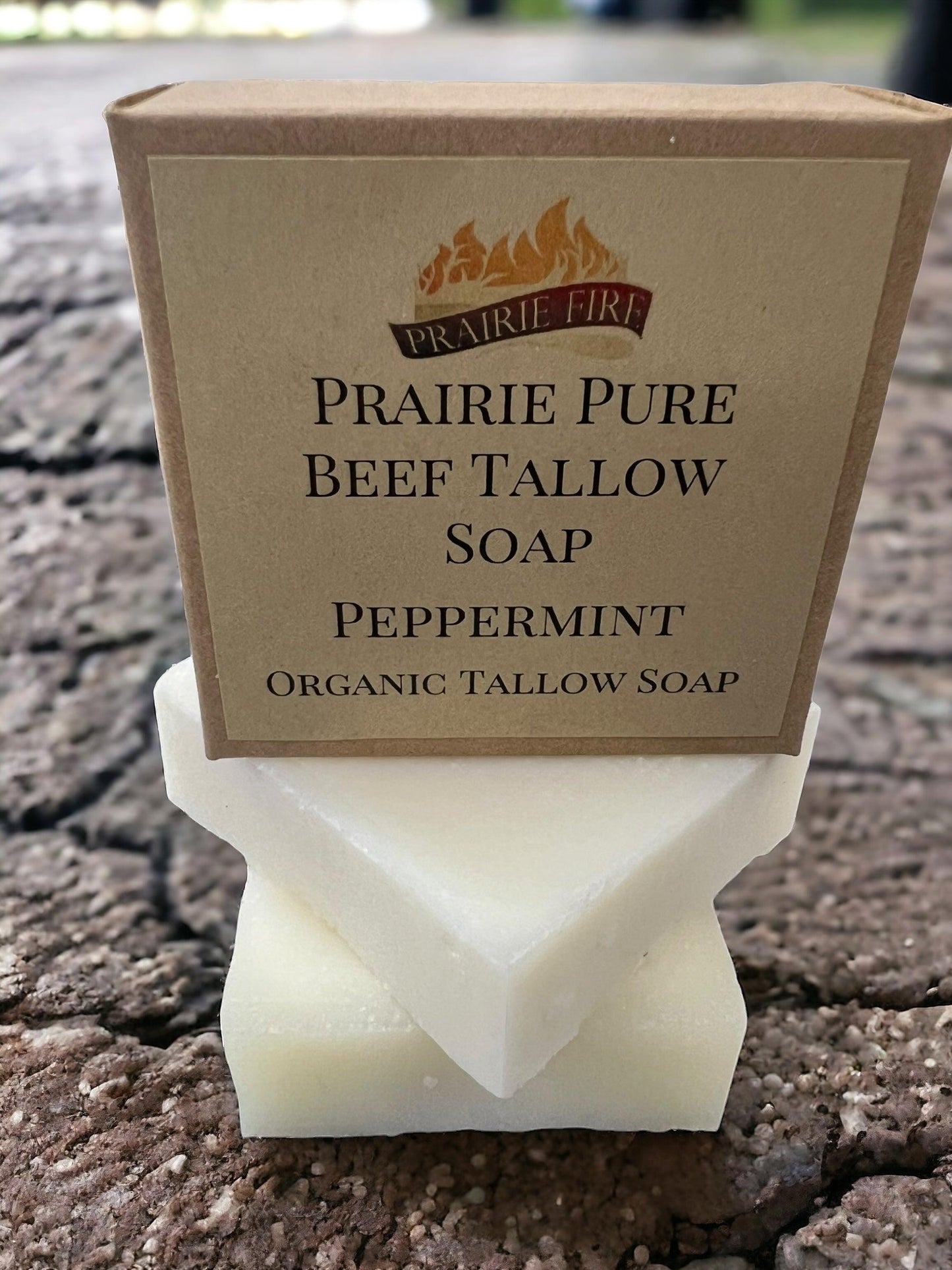 A pack of Prairie Fire Tallow, Candles, and Lavender Pure Beef Tallow Soap Bars (3 Pack), made in the USA from grass-fed and finished beef tallow, sits on a wooden surface with two white bars stacked below the packaging.