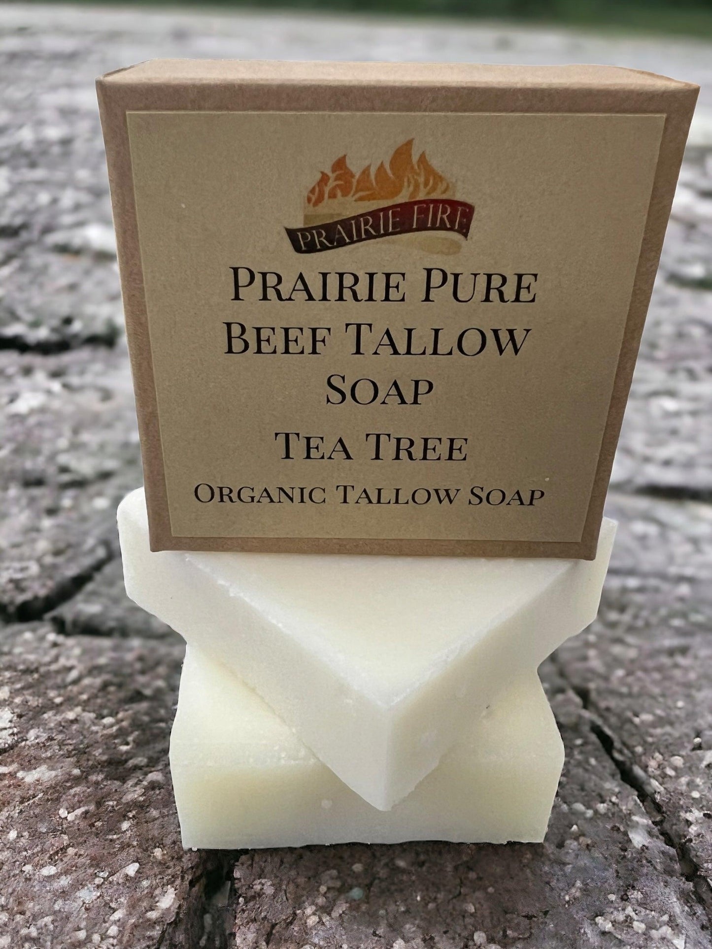 A box of Prairie Fire Tallow, Candles, and Lavender Pure Beef Tallow Soap Bar (3 Pack) sits atop two white soap bars on a rough stone surface. The soap is organic, grass fed and finished, for face, body, and hair. Made in the USA.