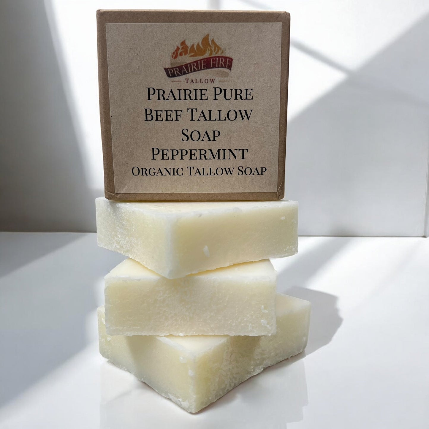 A bright, sunlit photo shows three creamy white Pure Beef Tallow Soap Bars by Prairie Fire Tallow, Candles, and Lavender—natural, organic, USA-made soaps for face, body, and hair that cleanse, moisturize, soothe, and hydrate.