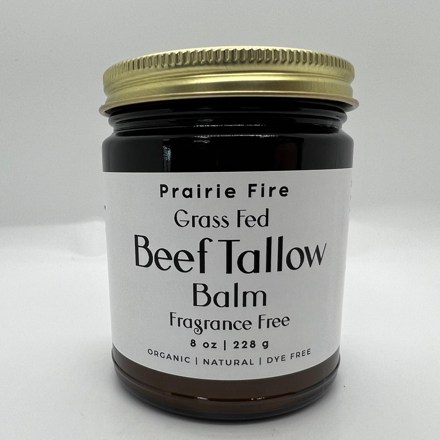 A brown glass jar with a gold lid labeled Prairie Fire Tallow, Candles, and Lavender Beef Tallow Balm - 8 oz sits on a white background. This organic, grass fed and finished moisturizer is made in the USA for nourishing skin care.