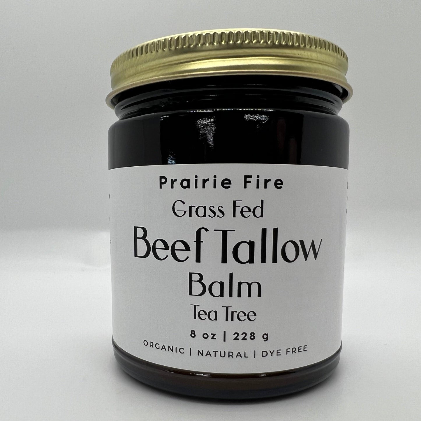 A dark glass jar with a gold lid, labeled Prairie Fire Tallow, Candles, and Lavender Beef Tallow Balm—8 oz, made in the USA from organic grass-fed beef tallow—is shown as a natural moisturizer against a plain white background.