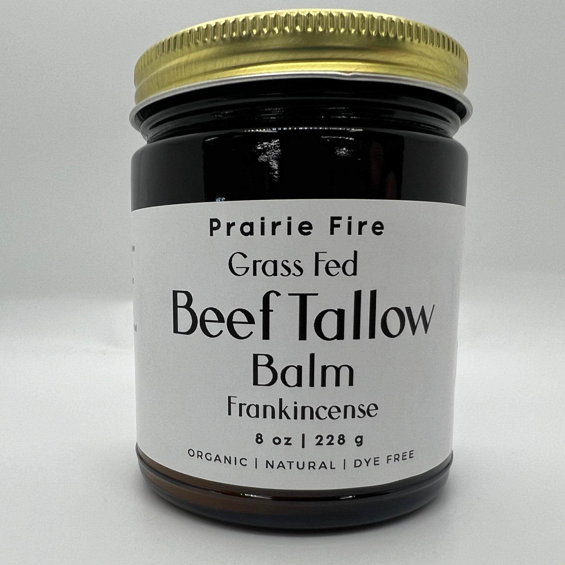 A dark glass jar with a gold lid labeled Prairie Fire Tallow, Candles, and Lavender Beef Tallow Balm - 8 oz. This organic, grass-fed moisturizer is made in the USA with dye-free ingredients for nourished skin. Shown on a plain white background.