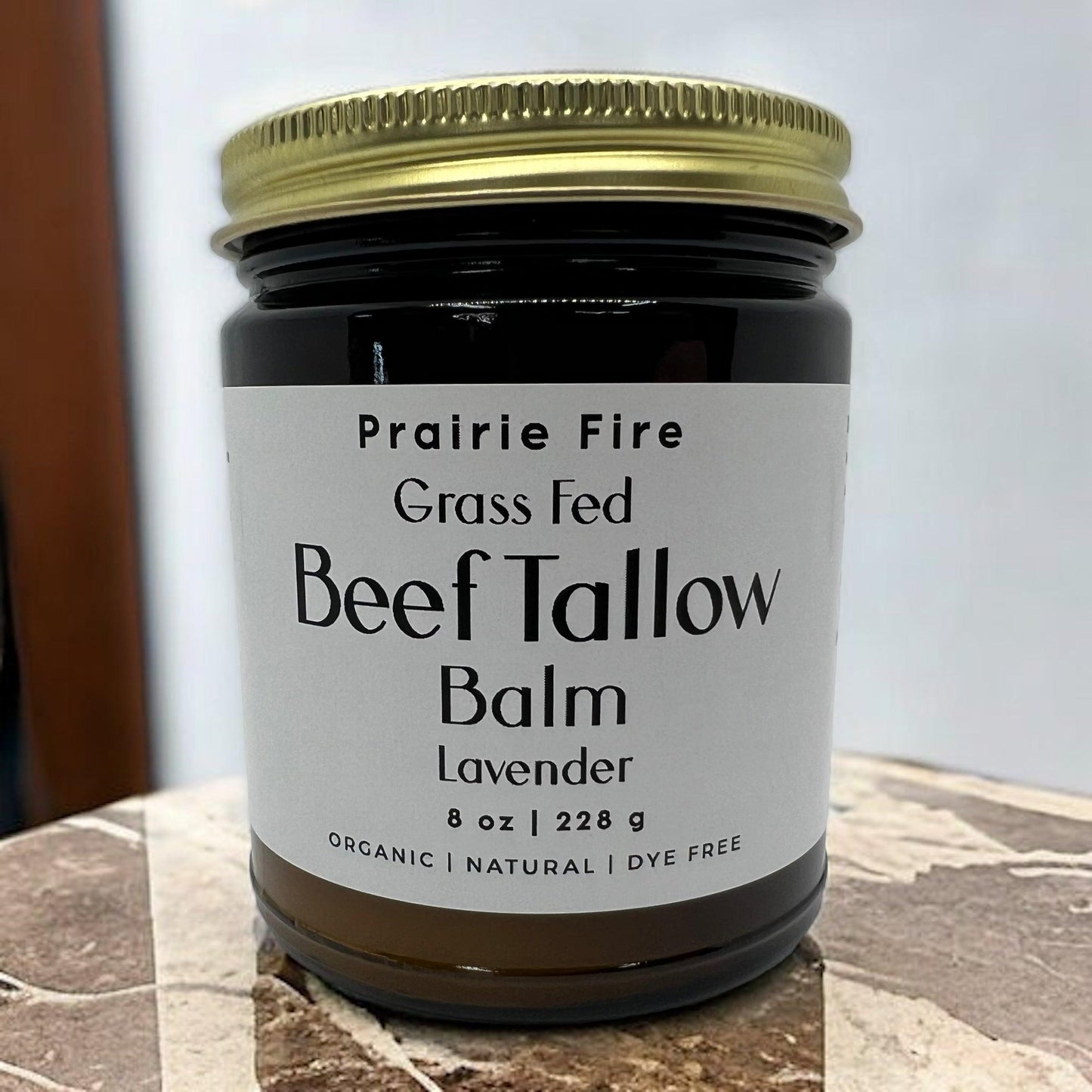 A jar of Prairie Fire Tallow, Candles, and Lavender Beef Tallow Balm (8 oz, organic, grass-fed & finished) rests on a marble surface with a gold lid and simple white label—a moisturizing skin care balm made in the USA.