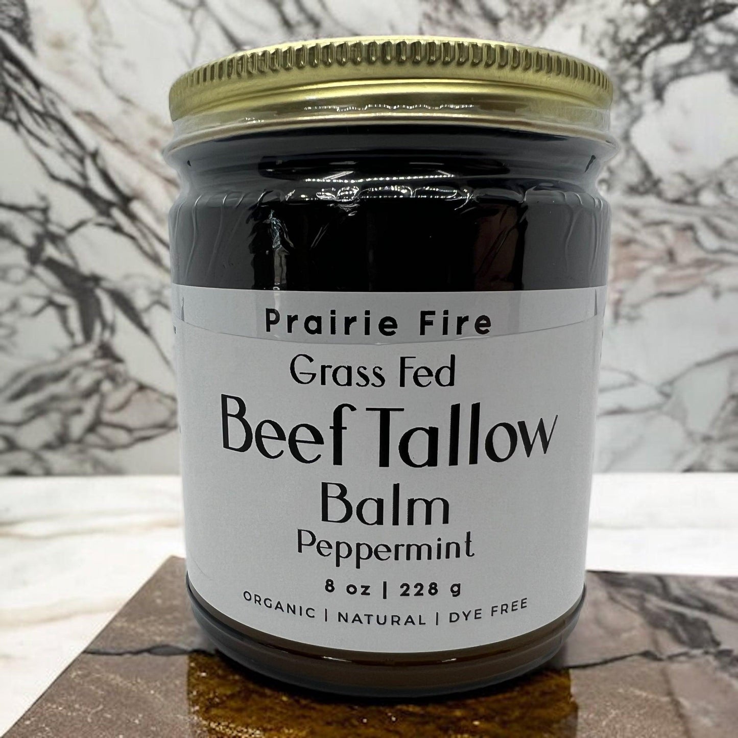 A glass jar of Prairie Fire Tallow, Candles, and Lavender’s Beef Tallow Balm (8 oz) sits on marble. The label notes it is organic, grass fed and finished, made in the USA, dye free, and a moisturizing skin care product.