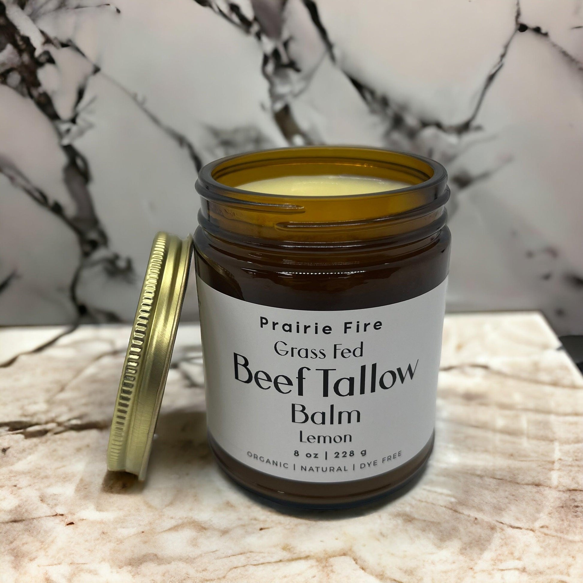An open amber jar of Prairie Fire Tallow, Candles, and Lavender Beef Tallow Balm (8 oz, organic grass-fed and finished, made in USA) with a gold lid sits on marble, spotlighting this natural moisturizing skin care product.