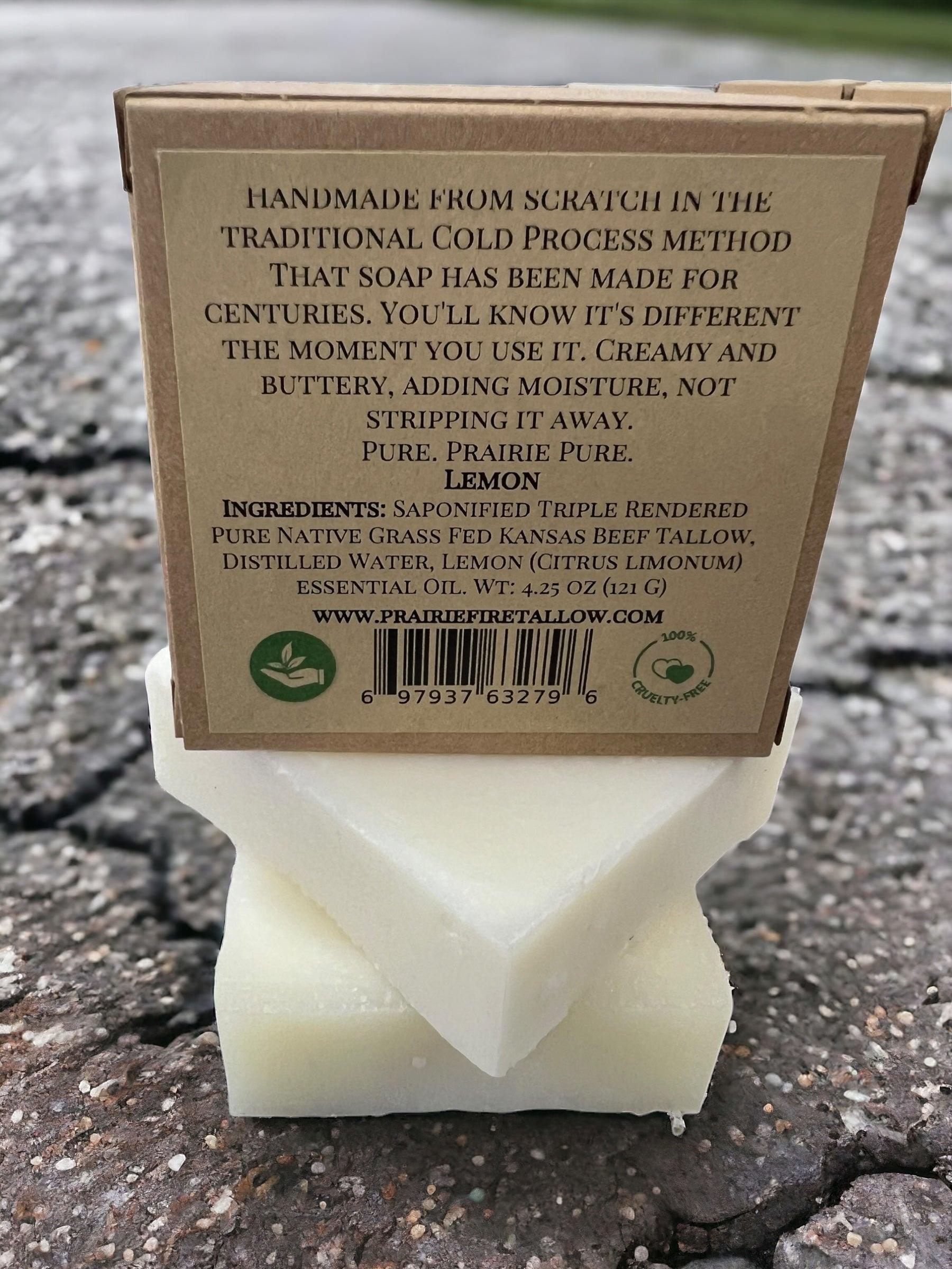 A Pure Beef Tallow Soap Bar by Prairie Fire Tallow, Candles, and Lavender with a brown label sits on cracked pavement. This natural, organic soap is handmade in the USA with grass-fed tallow and essential oils for face, body, and hair.