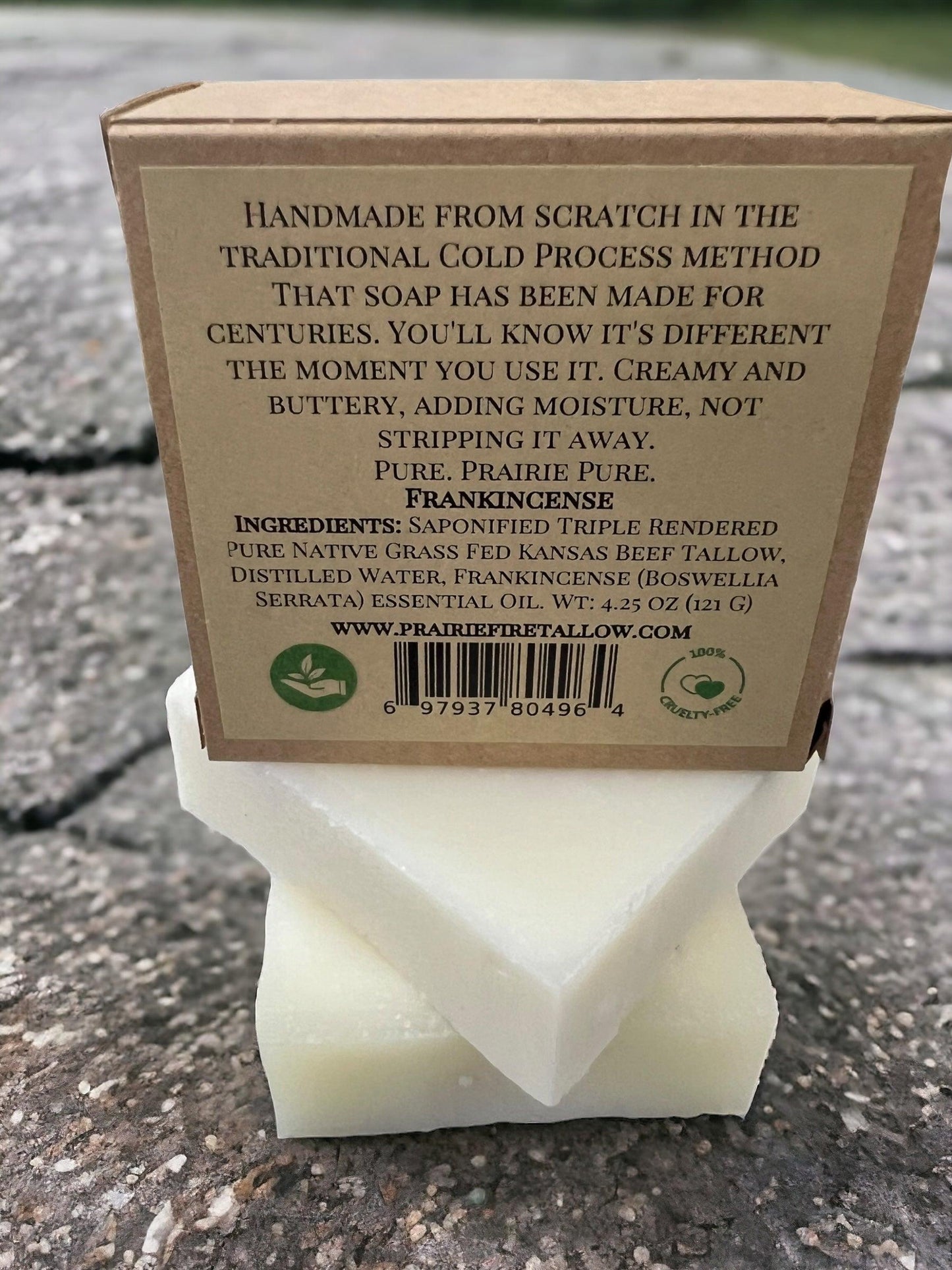 A Pure Beef Tallow Soap Bar by Prairie Fire Tallow, Candles, and Lavender sits on a white soap holder outdoors. This handmade, organic bar is grass fed, chemical free, and made in the USA for face, body, and hair.